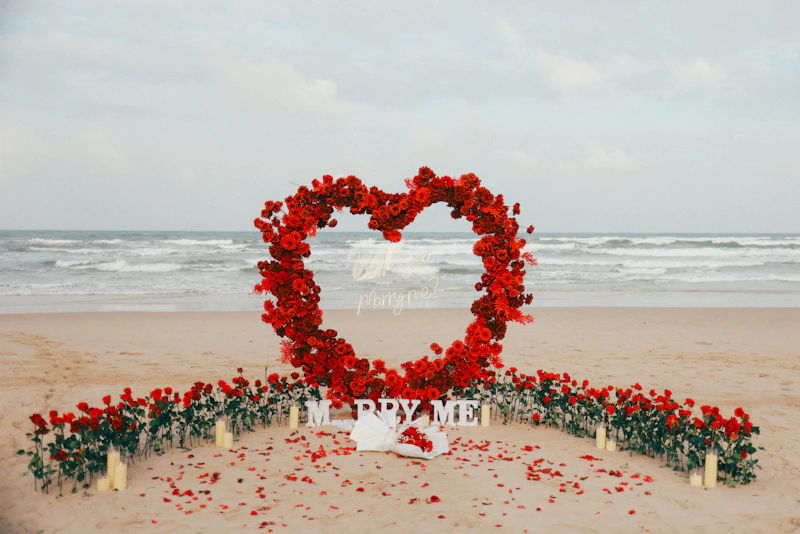 Heart-shaped floral arch with 'marry me' sign on beach.